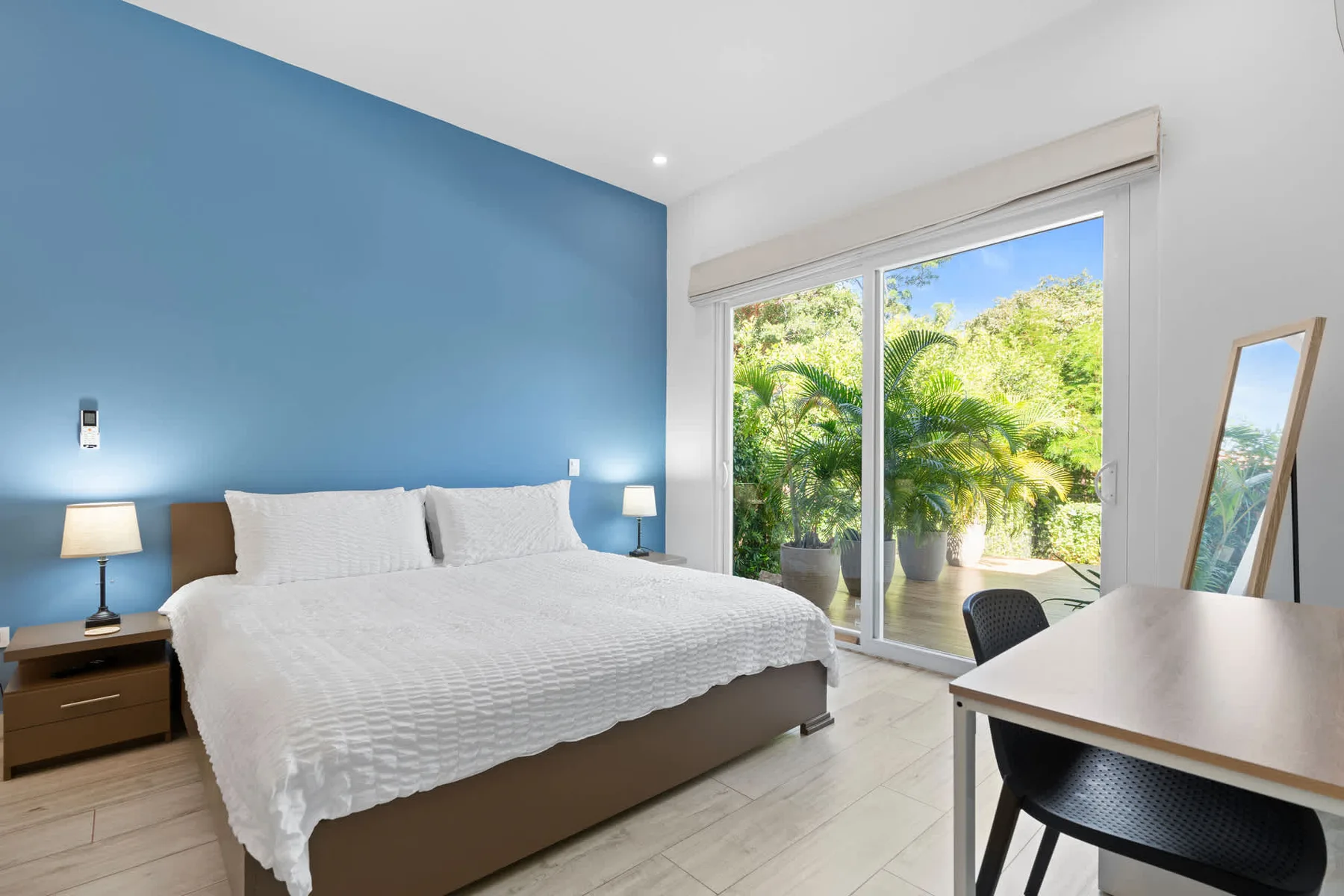 A bedroom with a large bed beside sliding glass doors overlooking greenery.