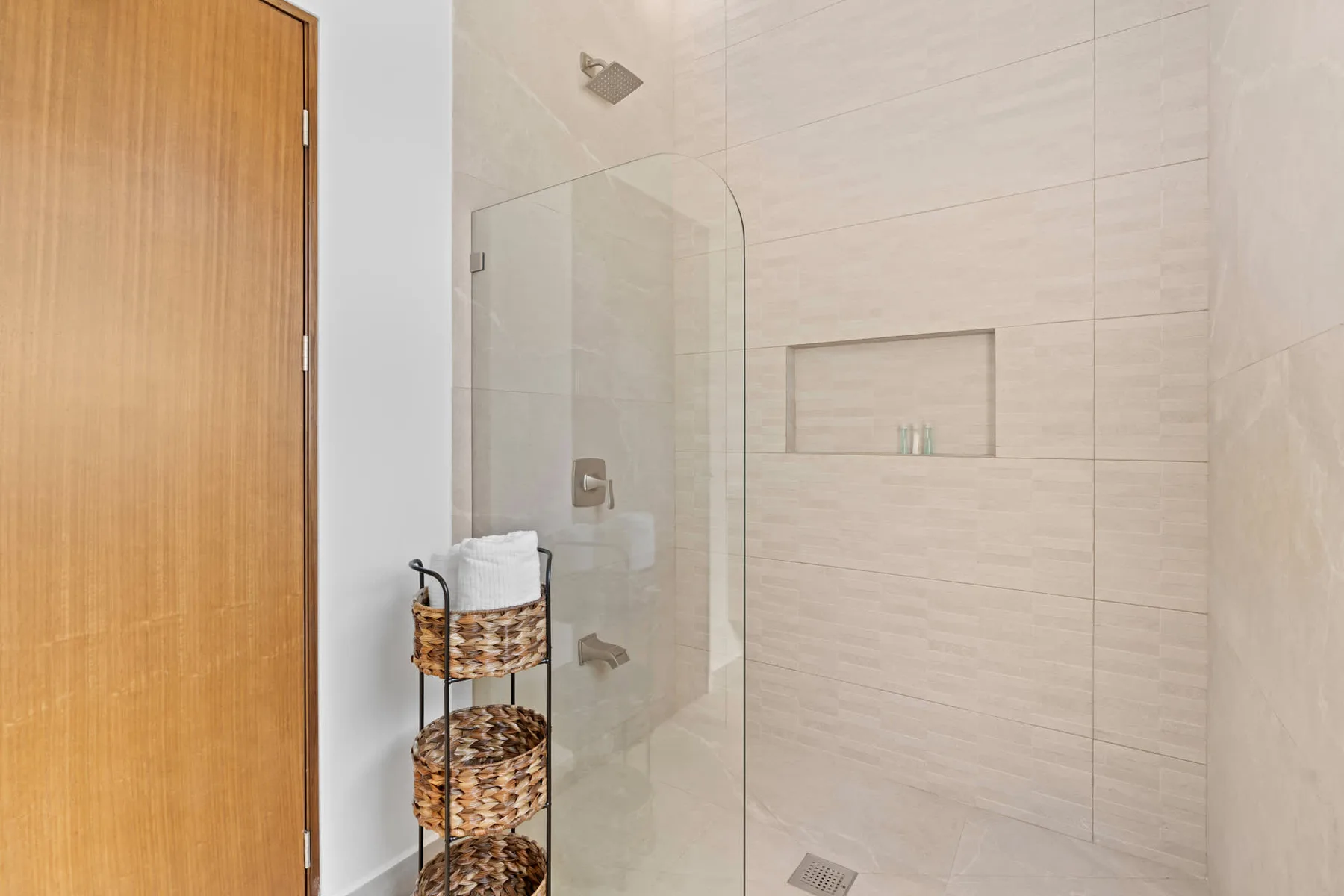 A tiled bathroom shower with a glass panel and recessed wall niche.