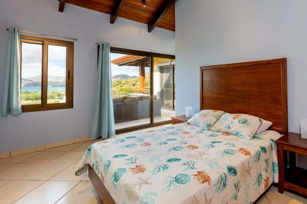 A bedroom with a bed covered in a pale floral-patterned bedspread.