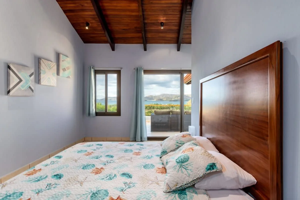 A bedroom with a patterned bedspread and a view through the open balcony door.
