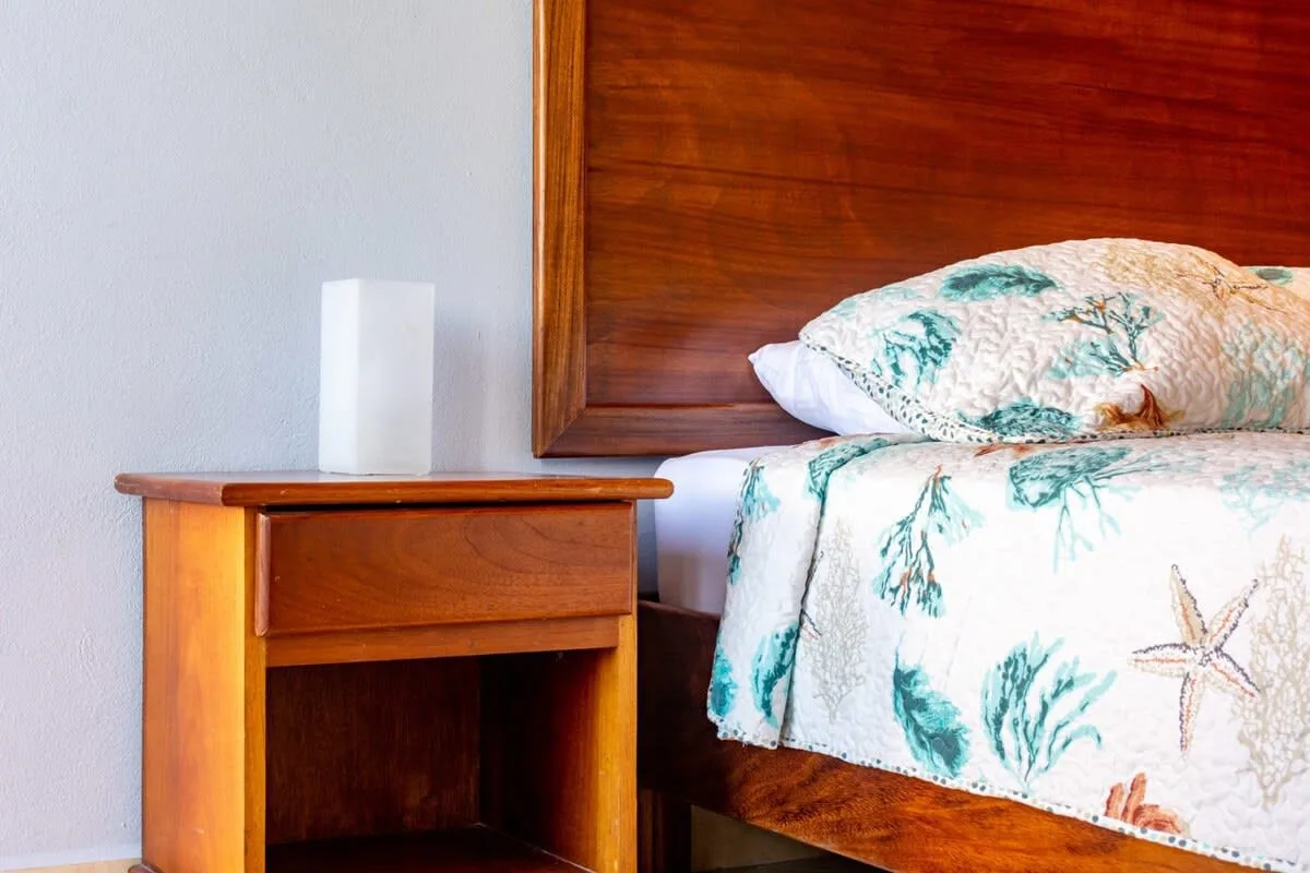 A bed with a patterned cover sits beside a wooden bedside table.