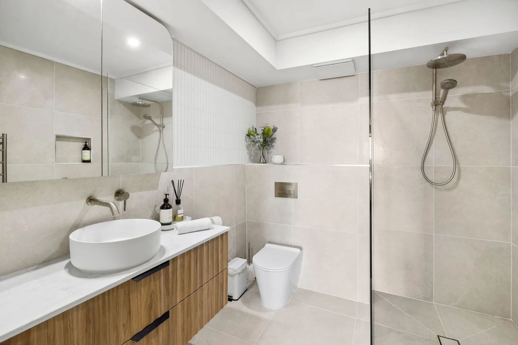 A modern bathroom with a vanity, toilet, and glass shower screen.
