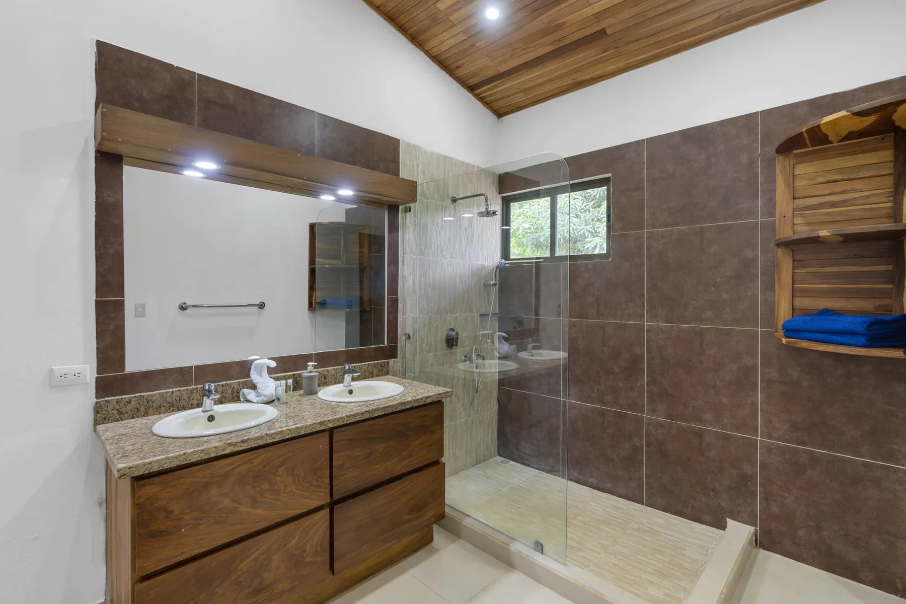 A tiled bathroom with a double vanity, large mirror, and glass shower.