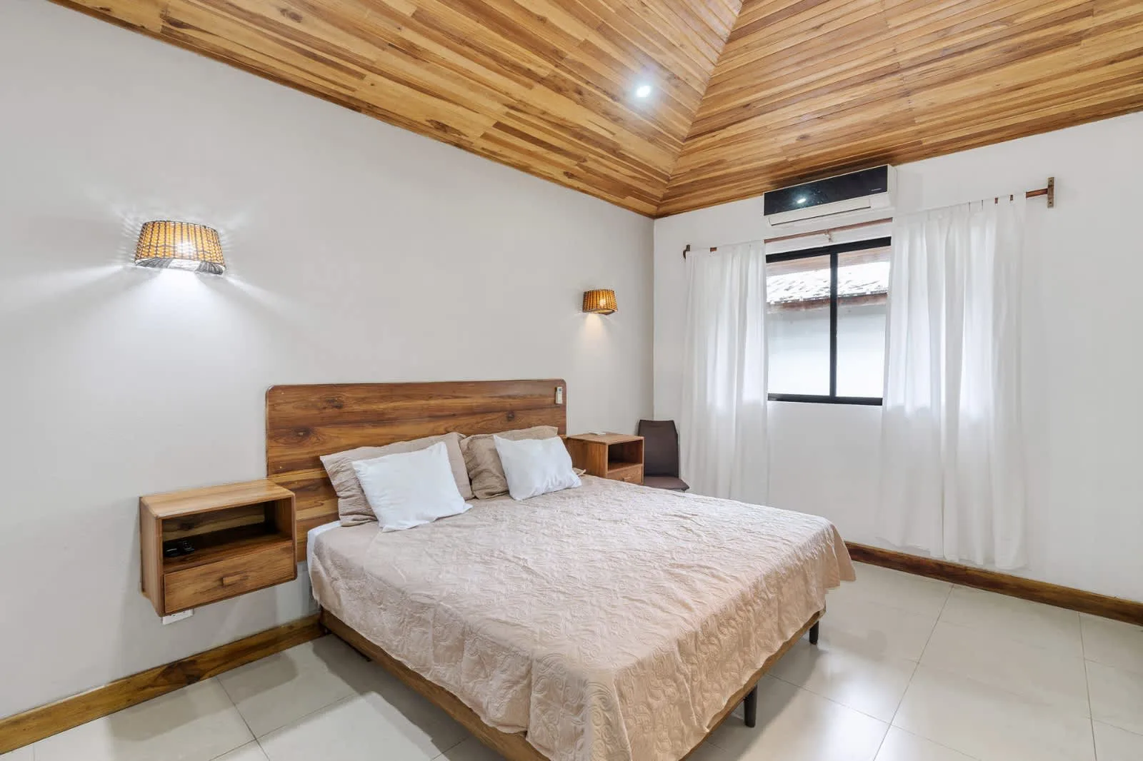 A bedroom with a double bed, bedside tables, and a window with curtains.