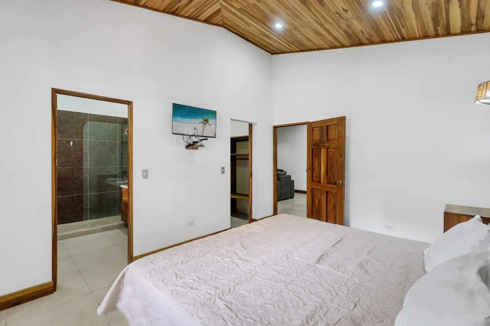 A bedroom with a bed, wood-paneled ceiling, and open doorways.