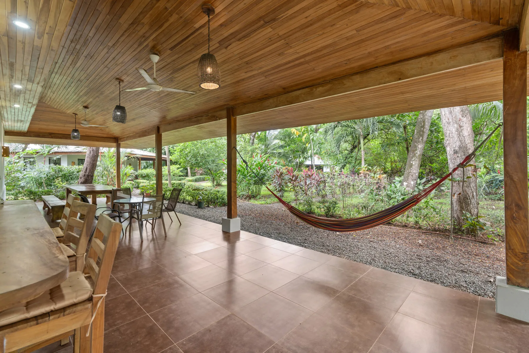 A covered outdoor dining area opens onto a garden, with a hammock strung between trees.
