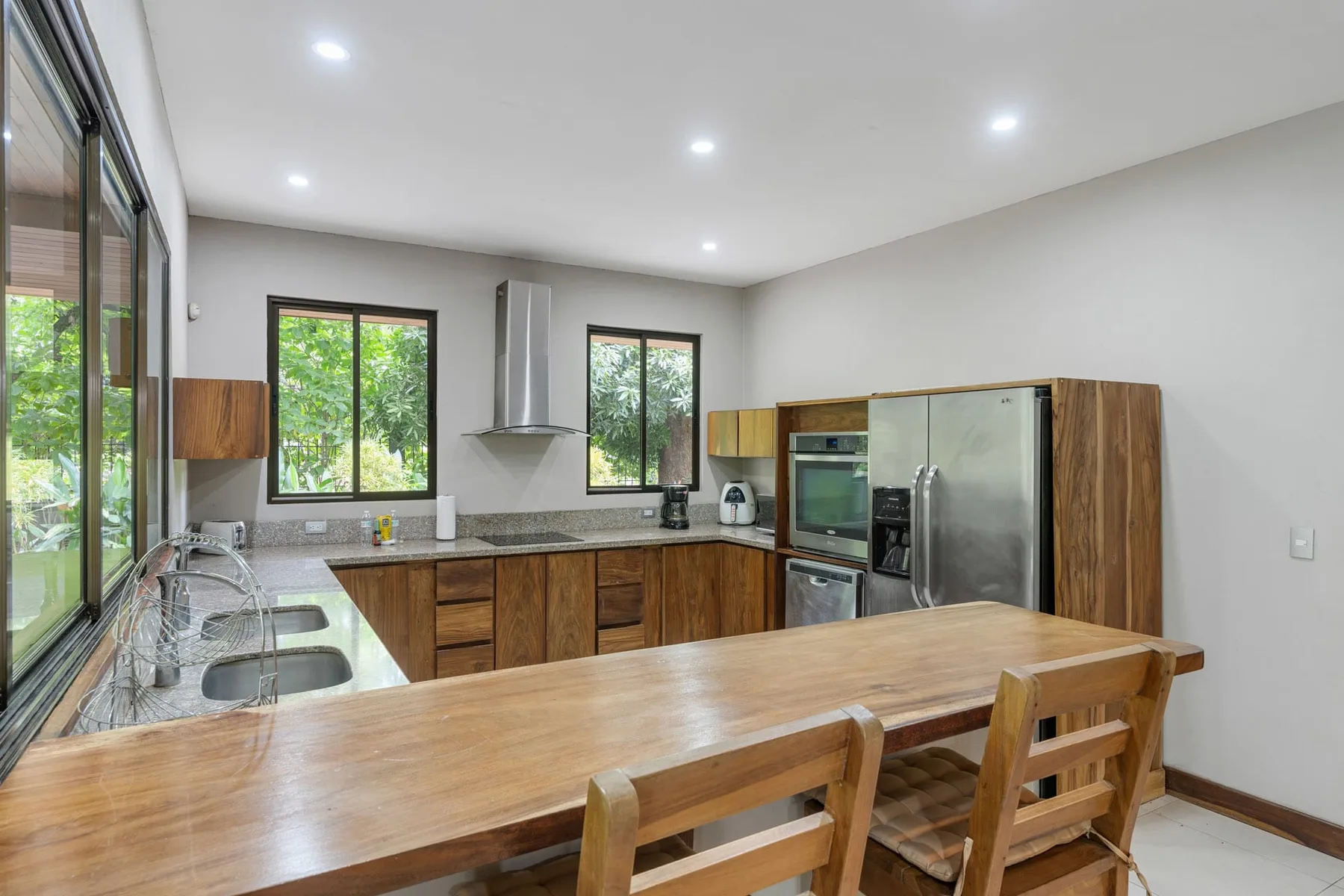 A bright kitchen with wooden cabinets, stainless steel appliances, and a long dining table.