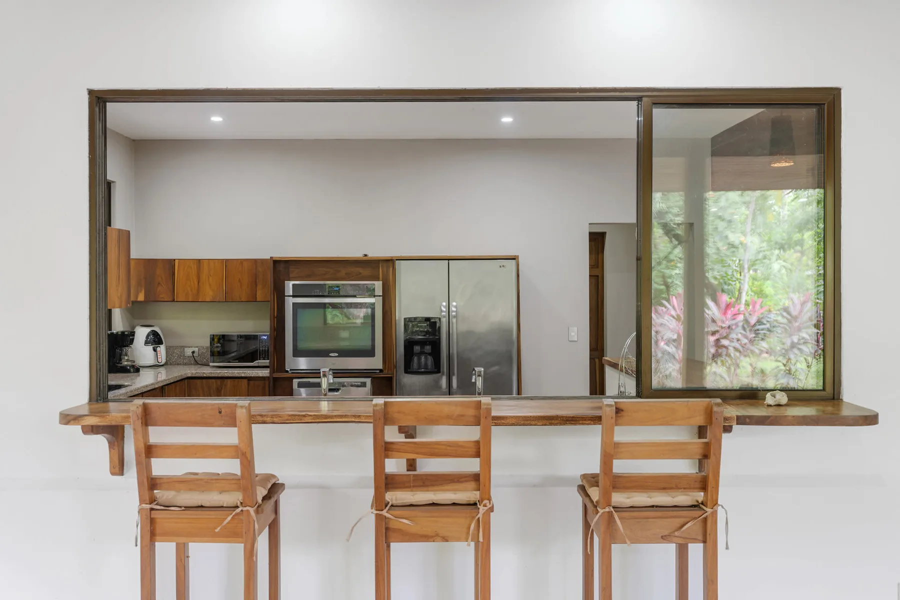 A kitchen opens onto a counter with wooden seating and a garden view.