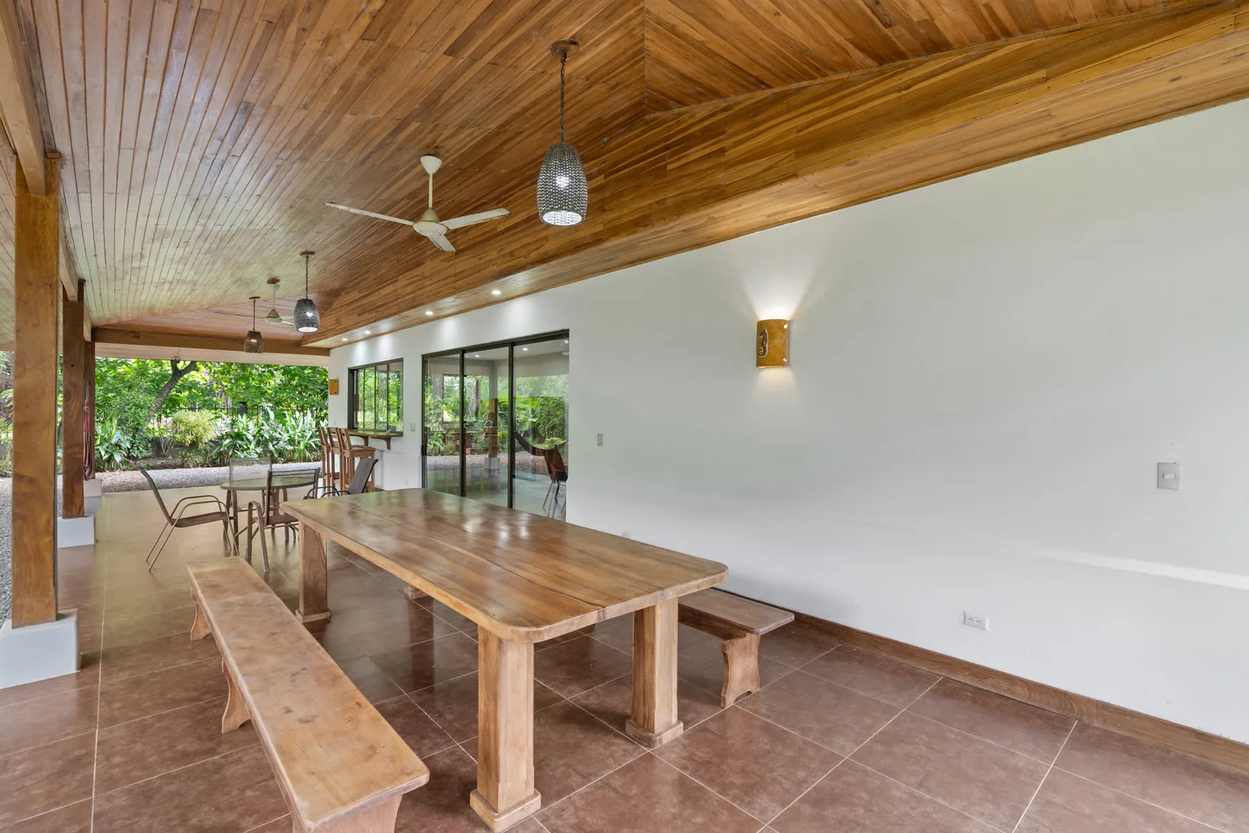 An open dining area with a long wooden table beneath a wood-paneled ceiling.