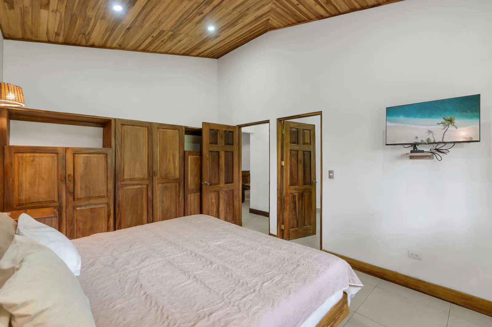 A bedroom with a bed, wooden wardrobes, and a television mounted on the wall.