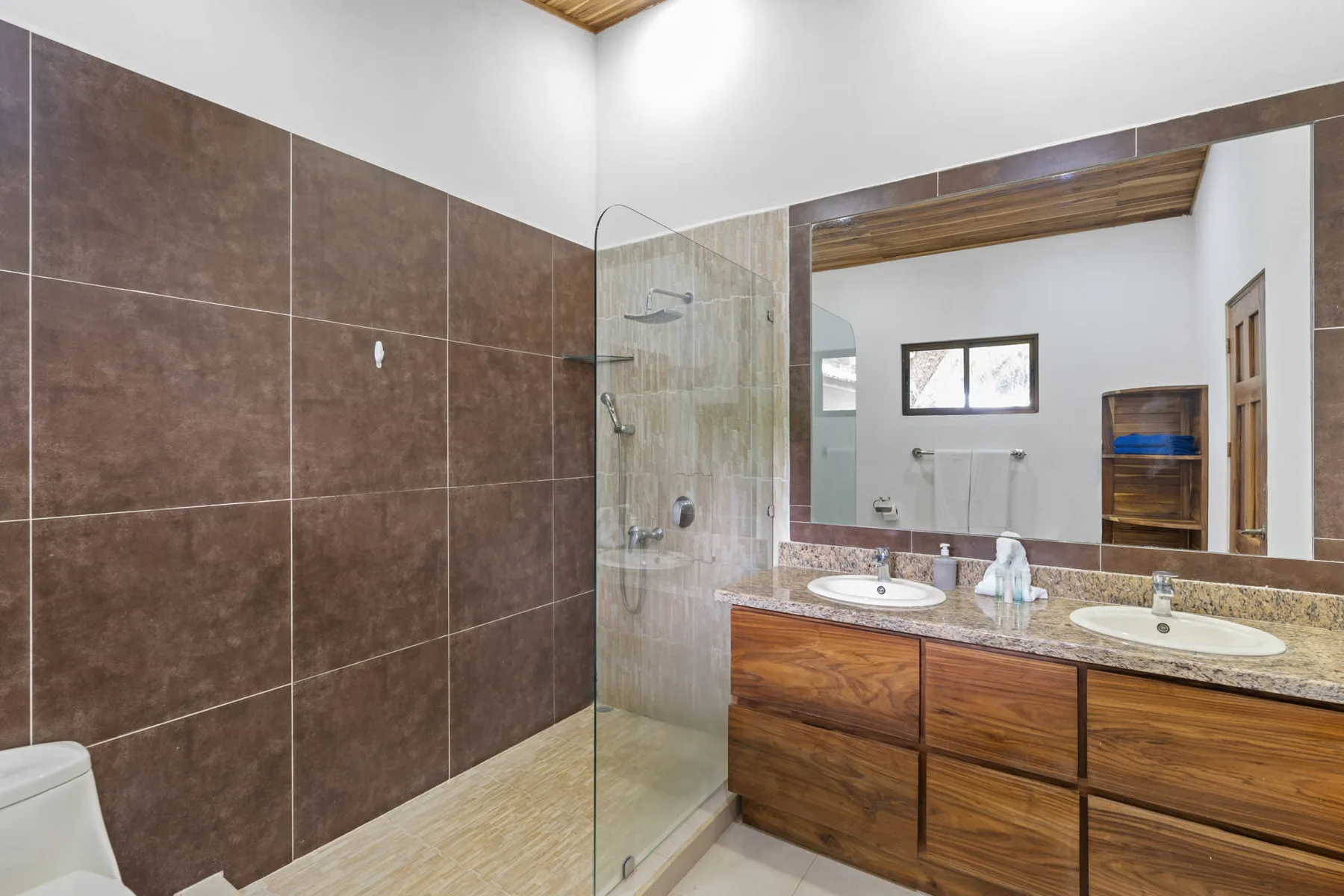 A bathroom with a glass shower, tiled walls, and a wide wooden vanity.