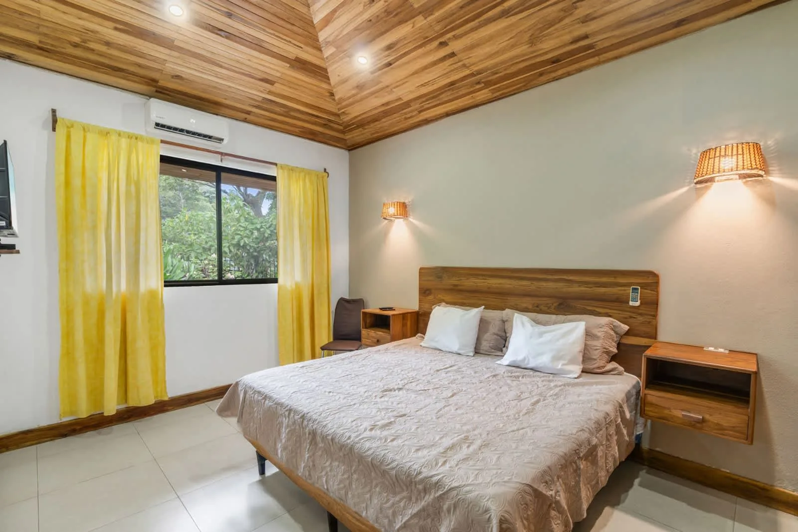 A bedroom with a large bed, yellow curtains, and a wood-paneled ceiling.