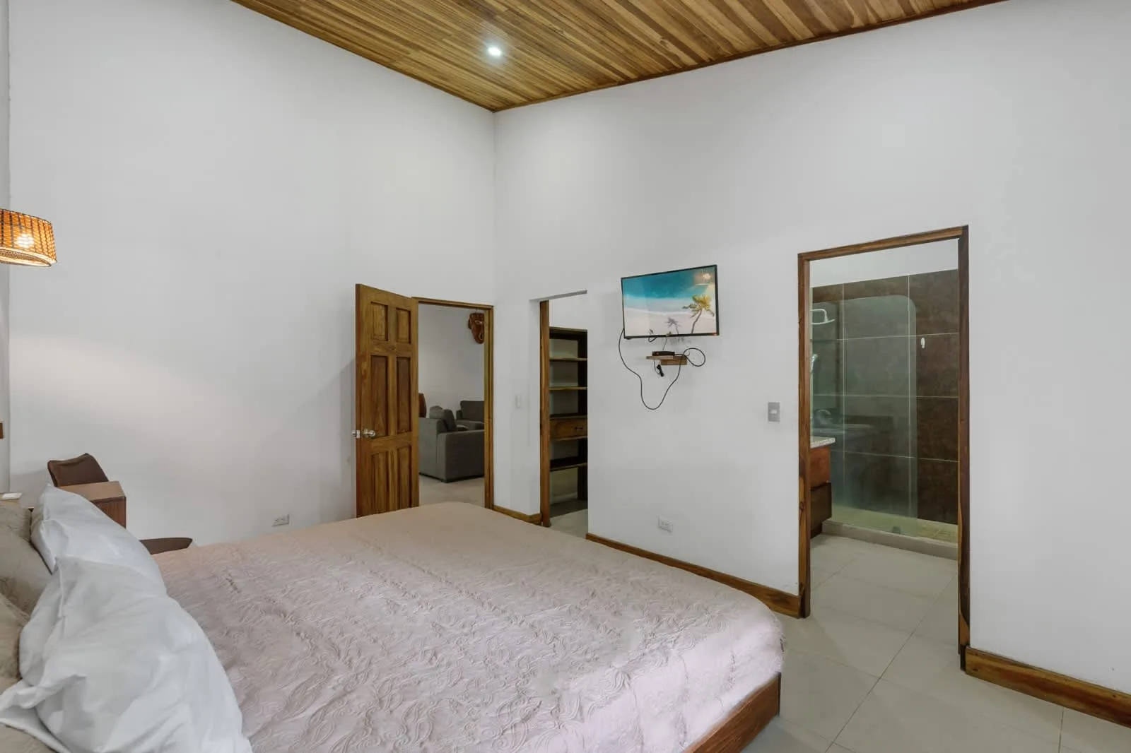 A bedroom with a bed, a wall-mounted television, and a doorway to the bathroom.