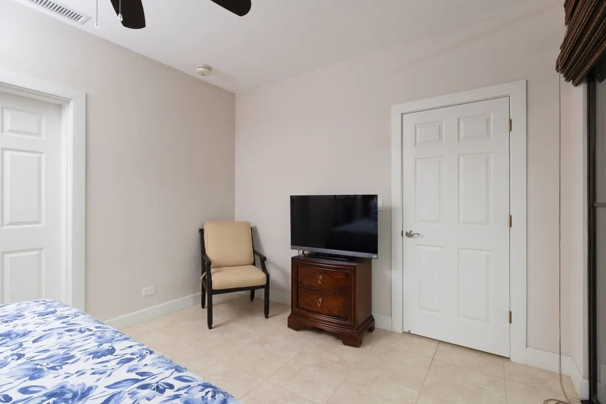 Un dormitorio con un televisor sobre un mueble de madera junto a una silla.