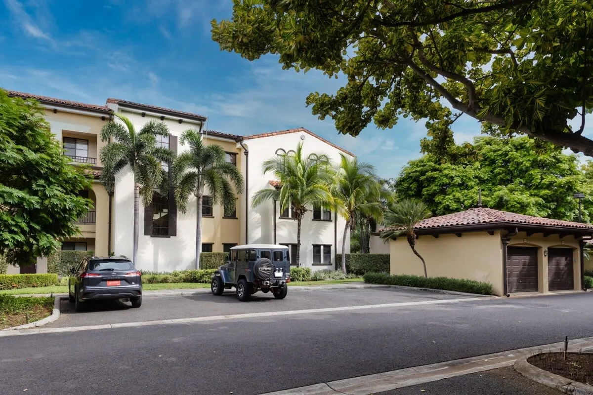 Zona común: Edificio residencial y vehículos estacionados junto a una entrada pavimentada bajo los árboles.