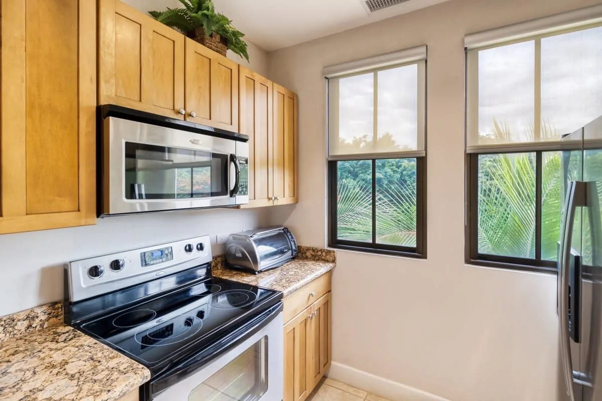 Una cocina con gabinetes de madera, una estufa y ventanas con vistas a la vegetación.