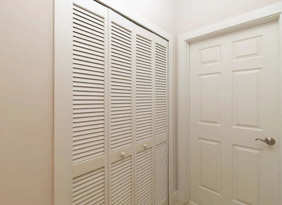 Un pasillo blanco con puertas de armario de lamas junto a una puerta panelada.