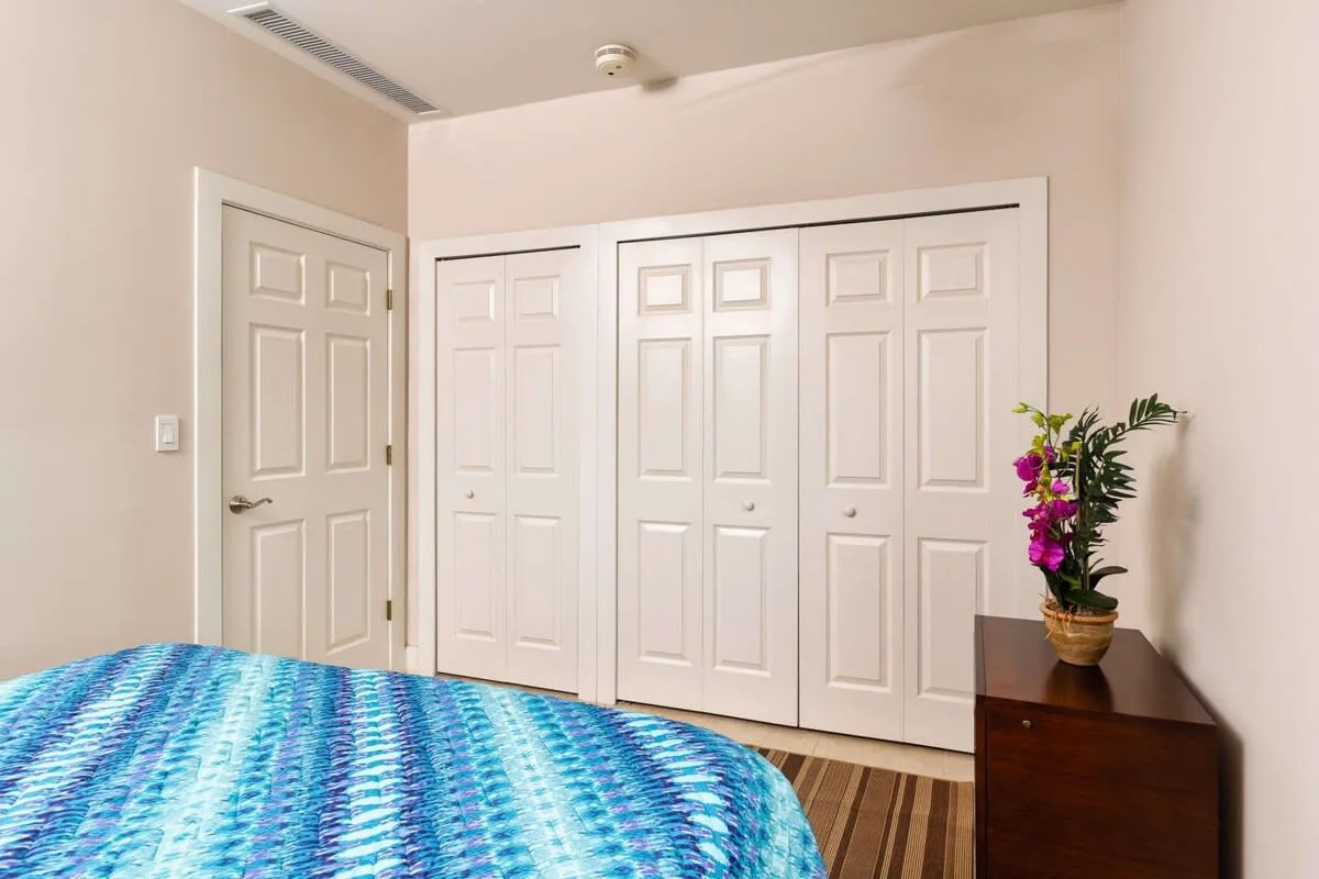 Dormitorio con una colcha azul estampada, puertas blancas y un arreglo floral.