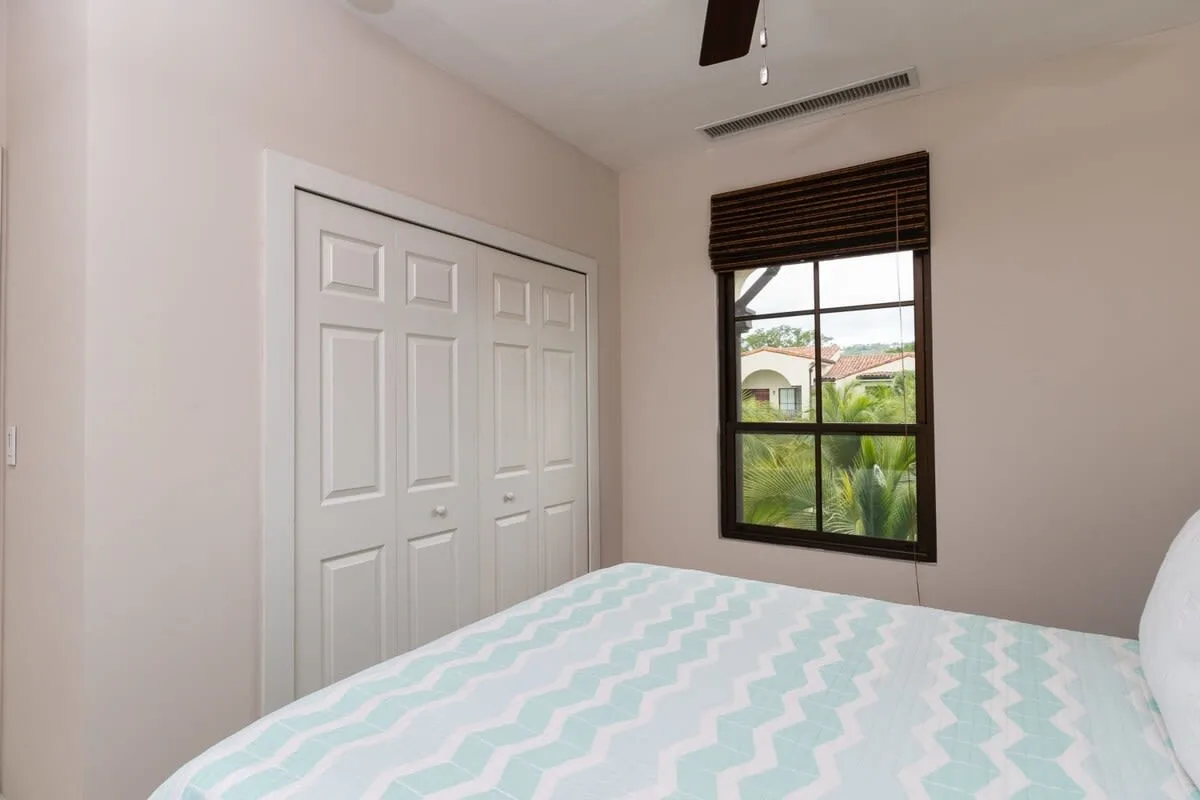 Un dormitorio con una cama, puertas de armario y una ventana con una persiana oscura.