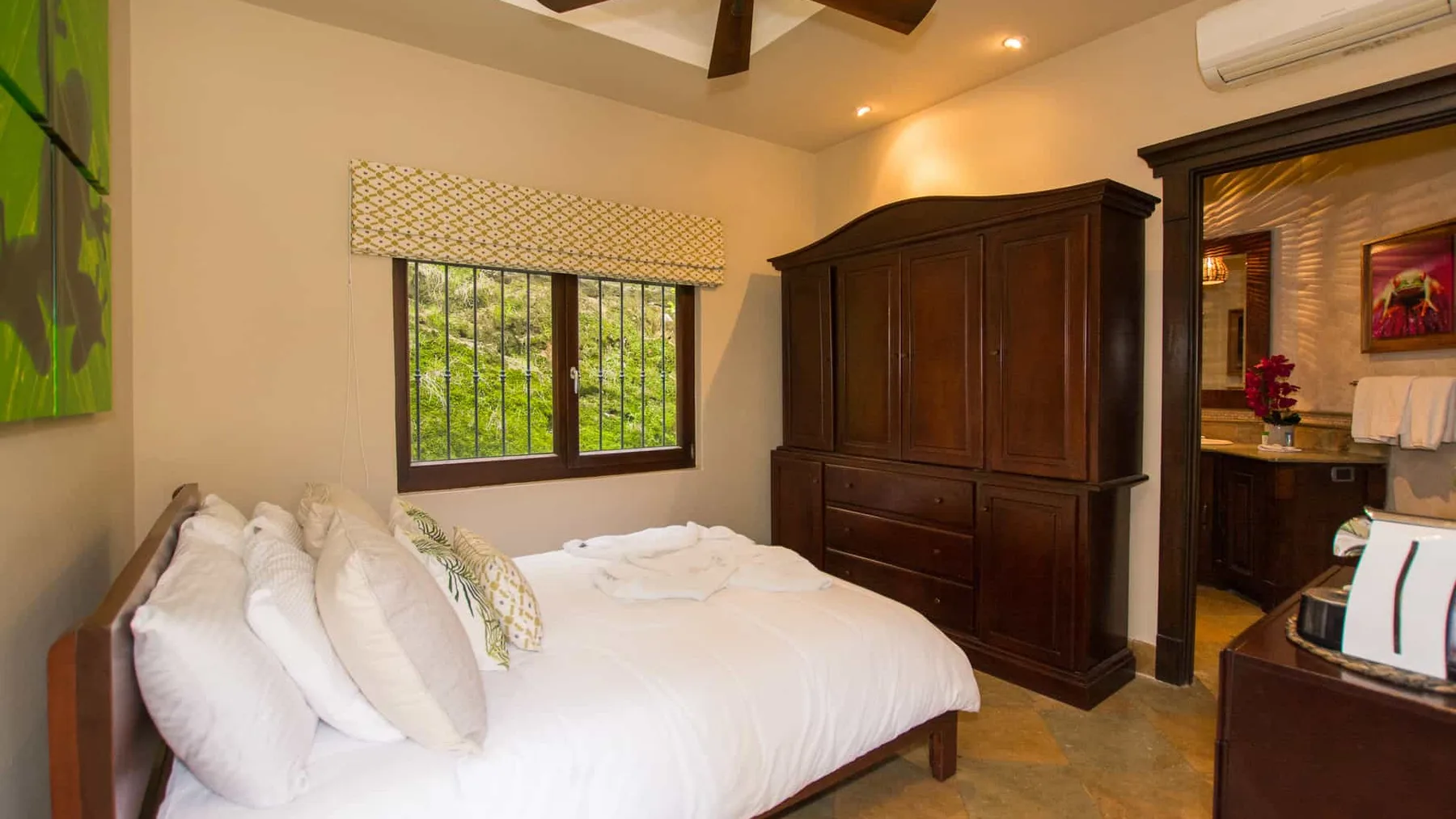 A bedroom with a bed, dark wooden wardrobe, and a window overlooking greenery.
