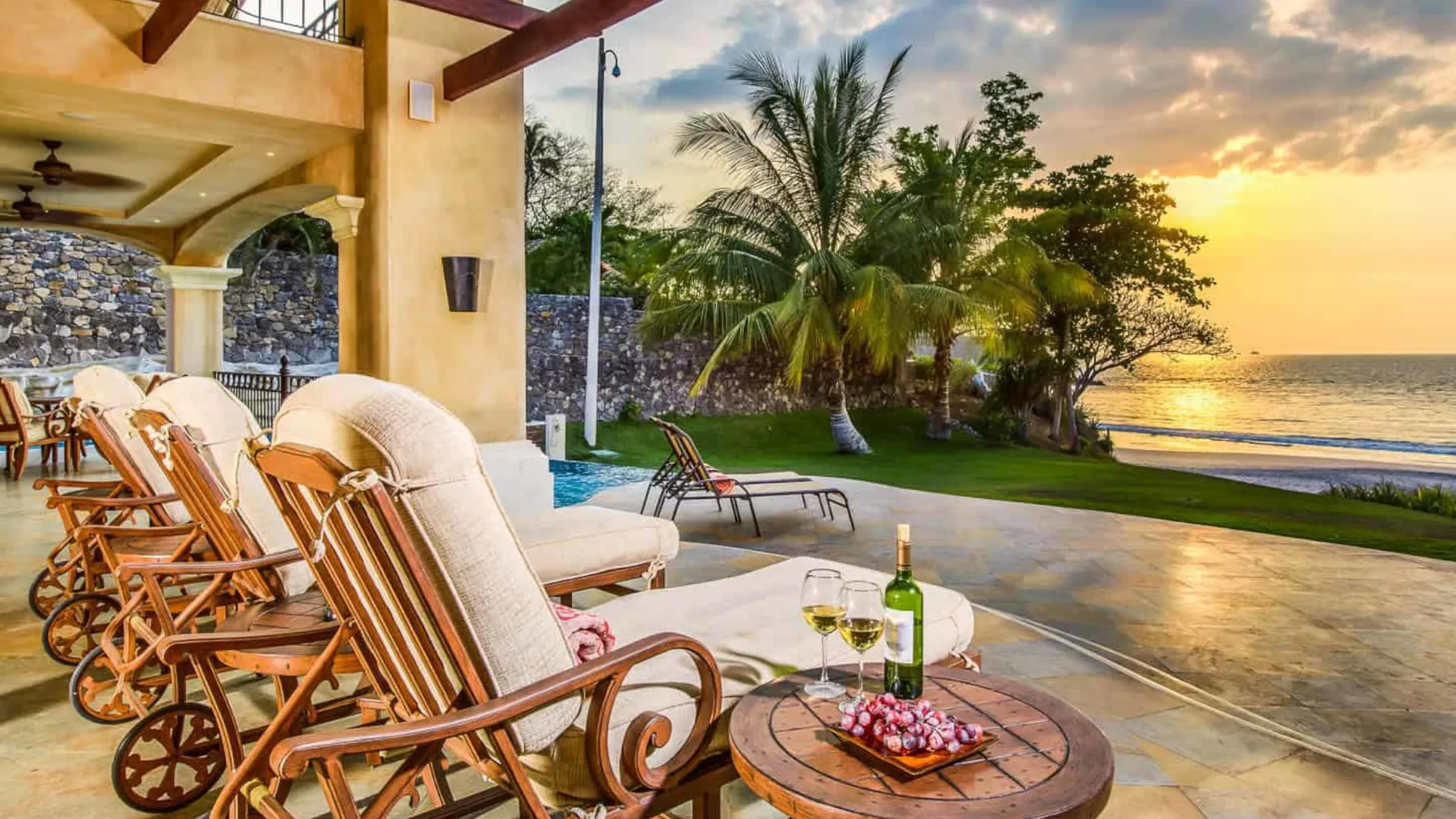 Outdoor poolside seating overlooks the ocean at sunset.