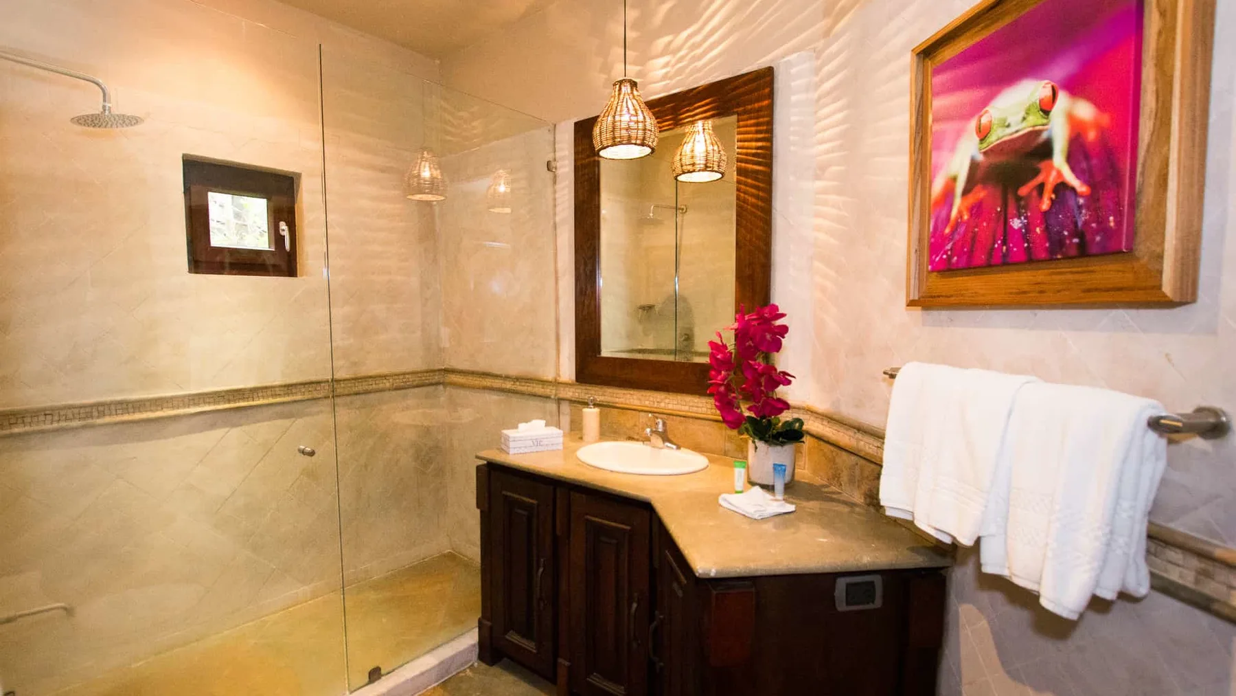 A bathroom with a glass shower, vanity, and colorful framed artwork.