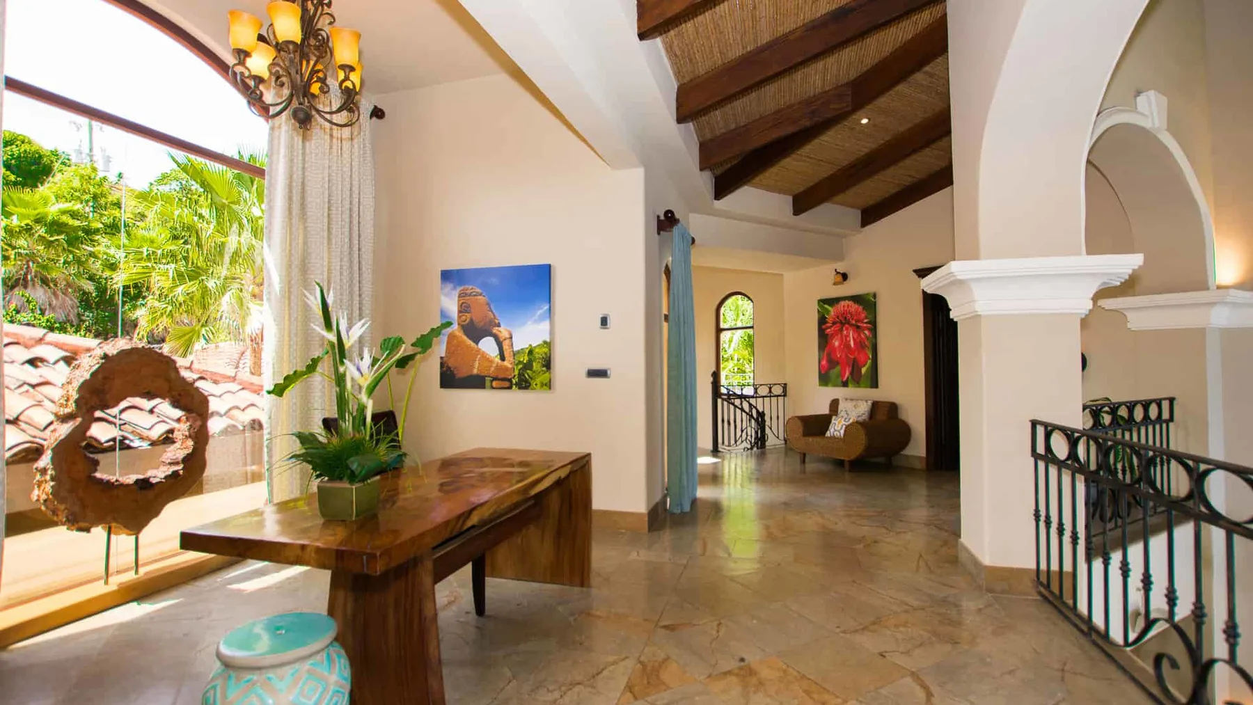 A spacious interior with a wooden table, tropical plants, and a staircase railing.