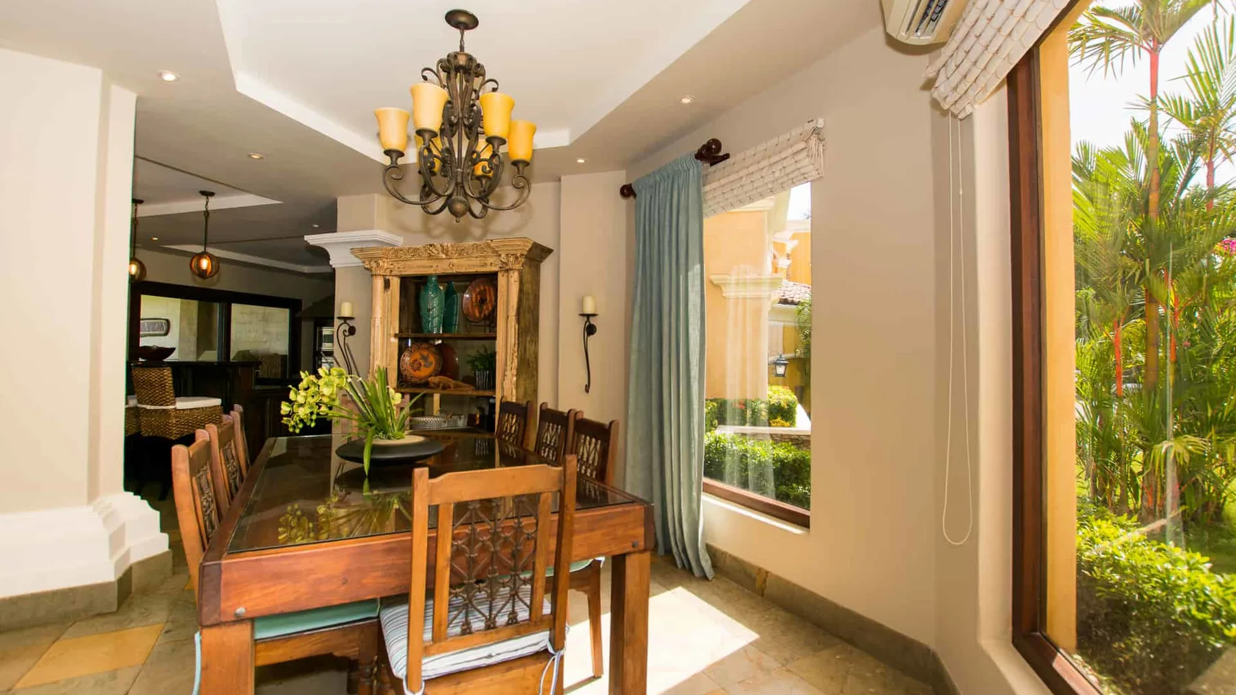 A dining area with a wooden table and chairs beside large windows.