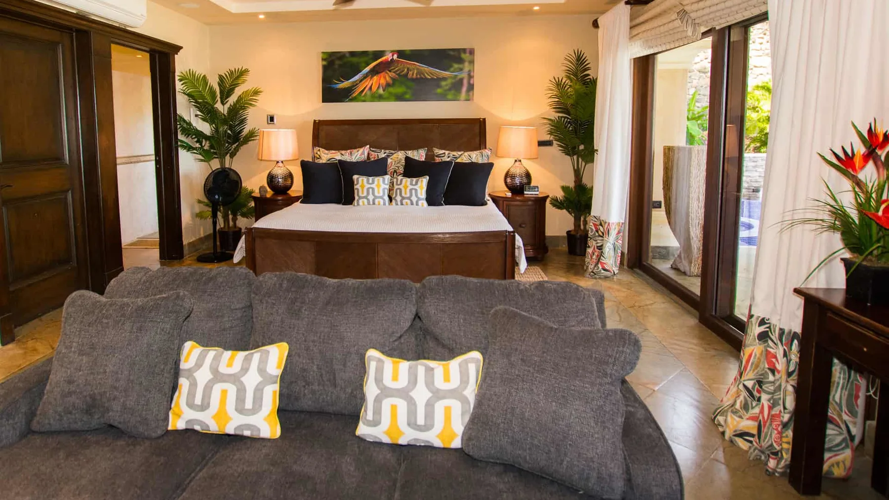 A bedroom with a bed behind a gray seating area and large glass doors.