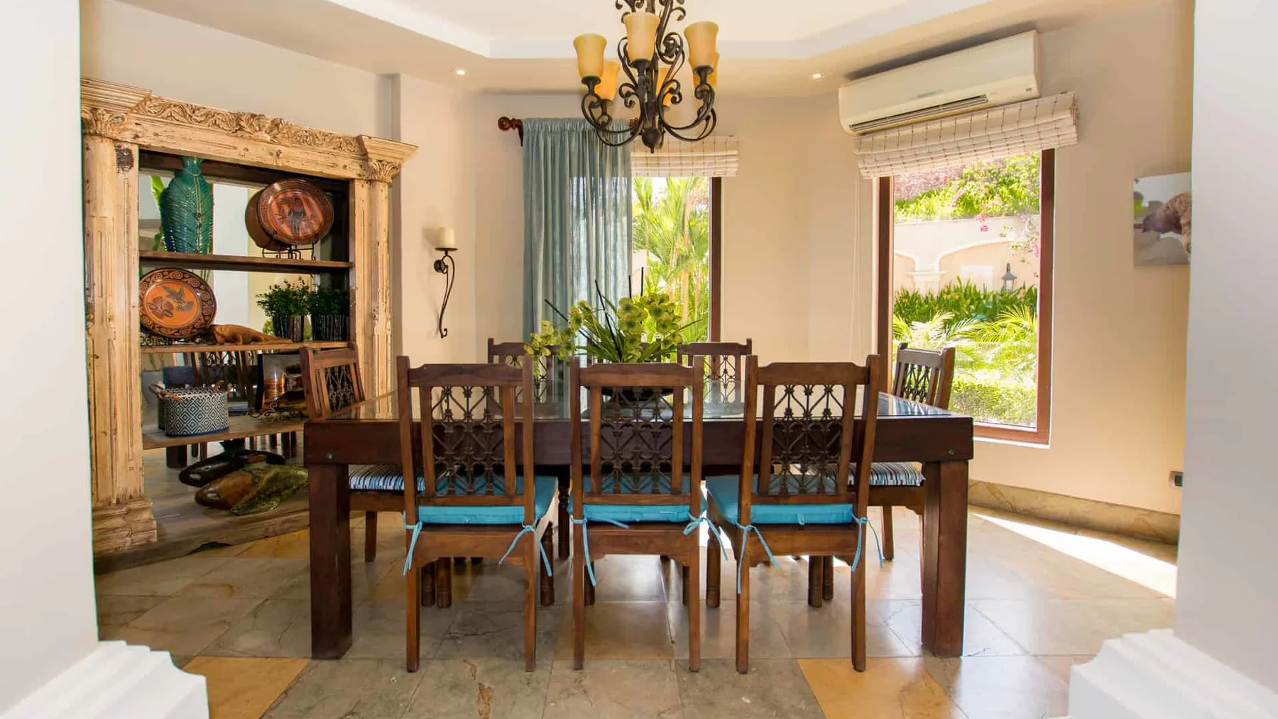 A dining room with a long wooden table and chairs beside large windows.