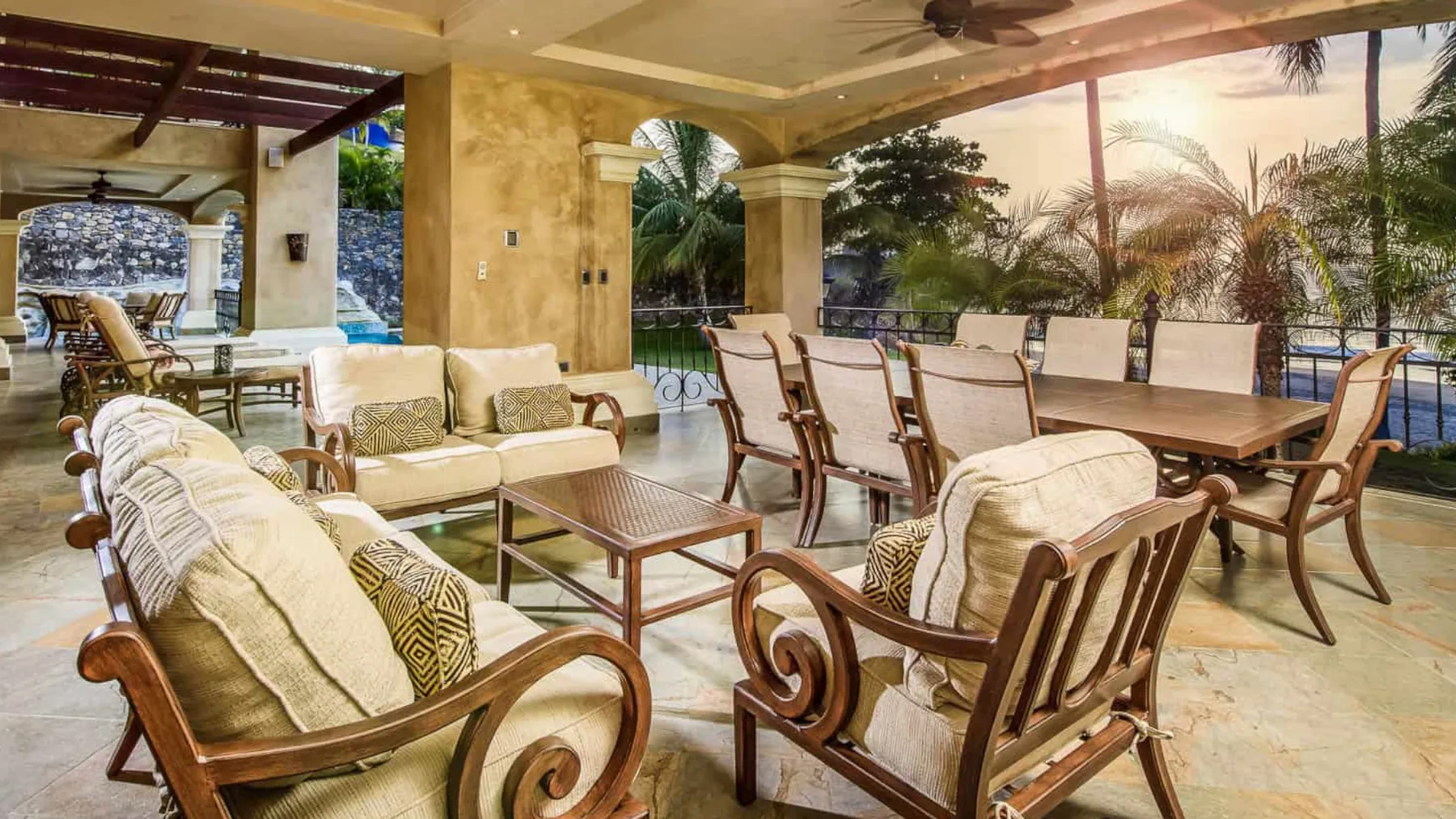 A covered outdoor dining and seating area with a table and cushioned chairs.