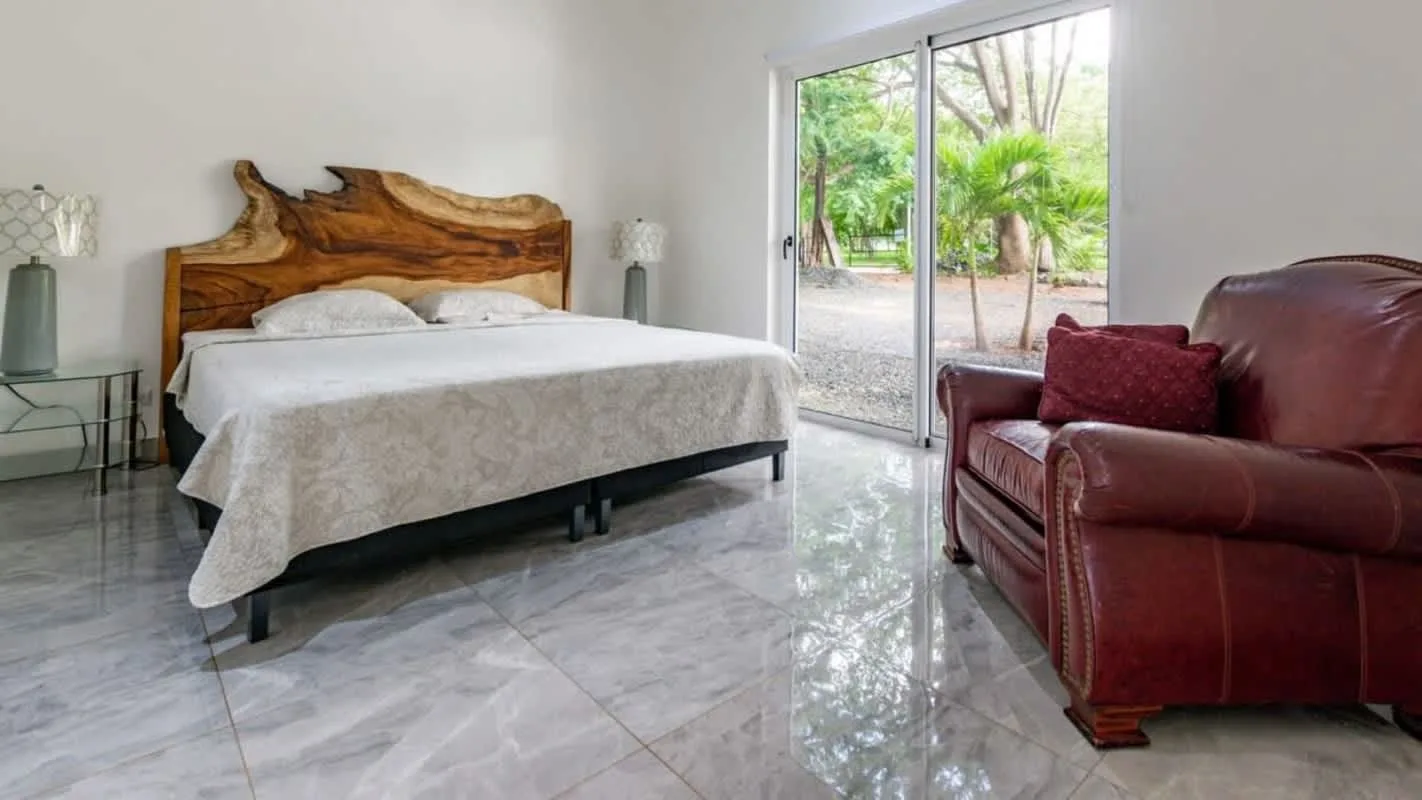 A bright bedroom with a bed, a leather armchair, and sliding glass doors.