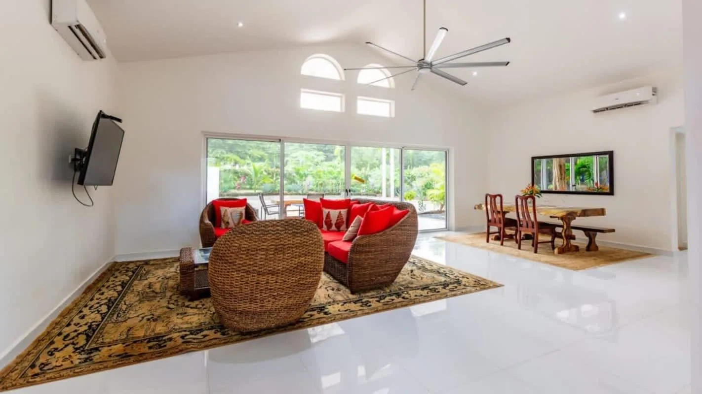 A bright living area has wicker seating on a patterned rug beside large windows.