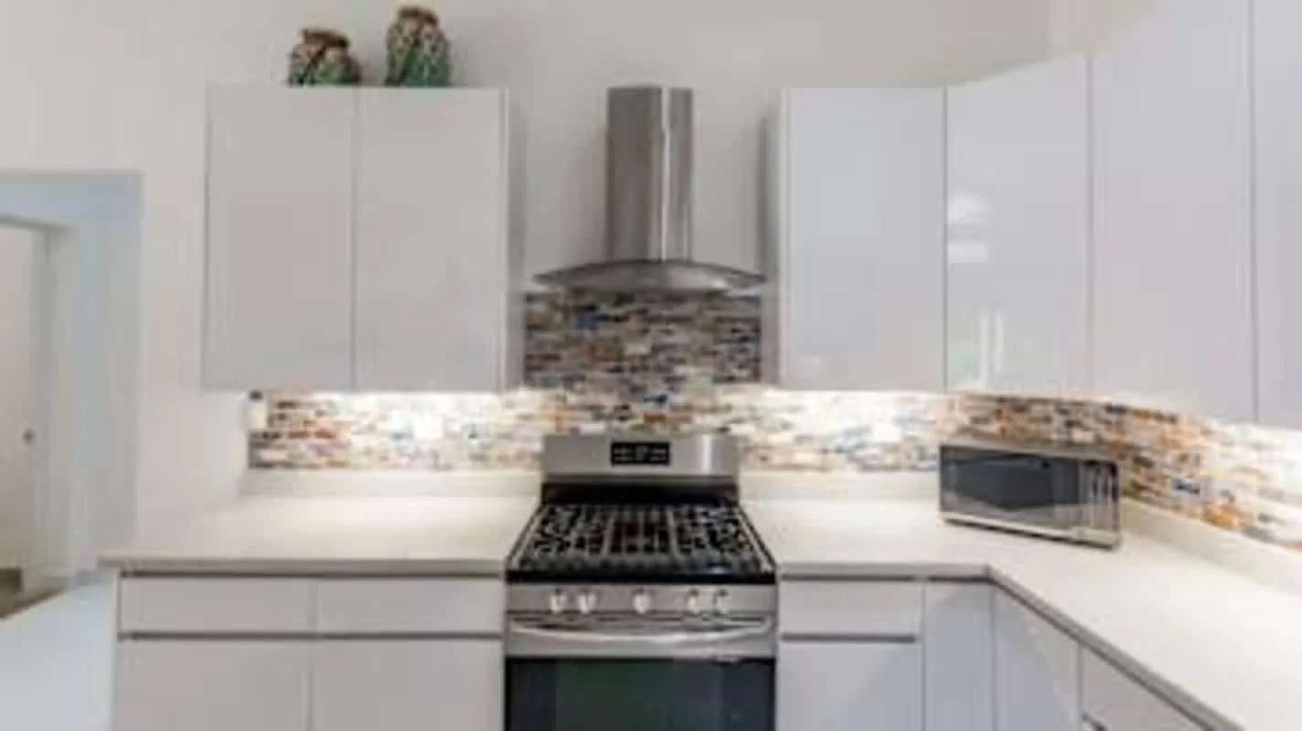 A modern kitchen with white cabinetry, a central range, and a tiled backsplash.