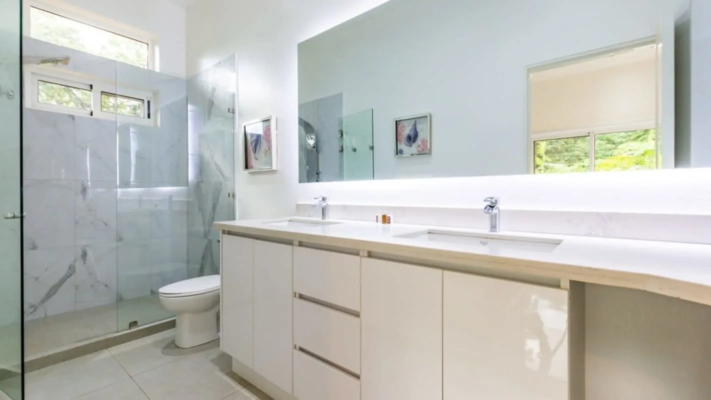 A bright bathroom with a long vanity, wide mirror, and glass shower.