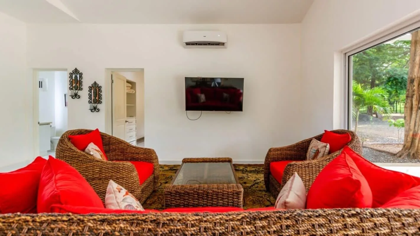 A living room with wicker seating, bright red cushions, and a glass-topped coffee table.