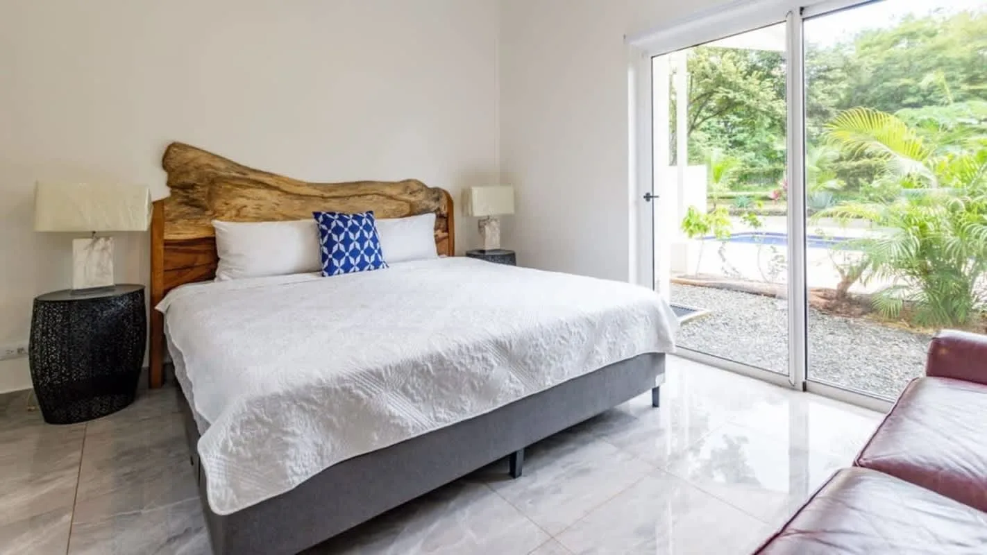 A bedroom with a bed beside a large glass door overlooking greenery.