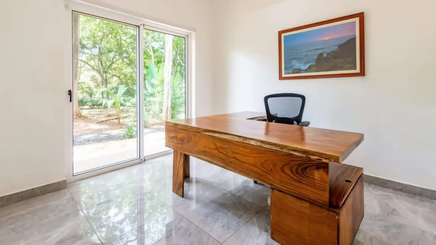 A wooden desk sits in a bright room beside sliding glass doors.