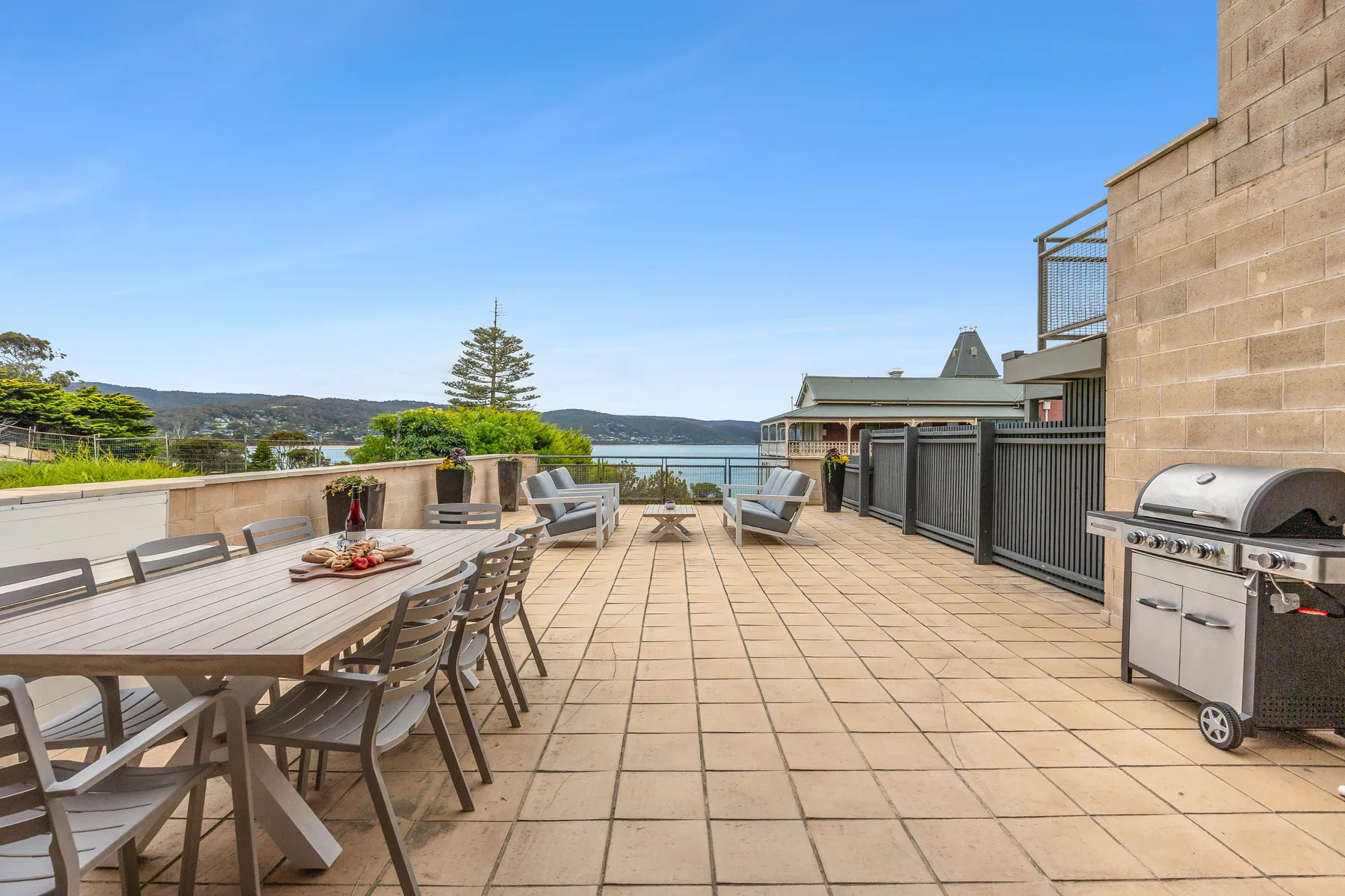 A spacious outdoor terrace has dining seating, a barbecue, and views toward the water.