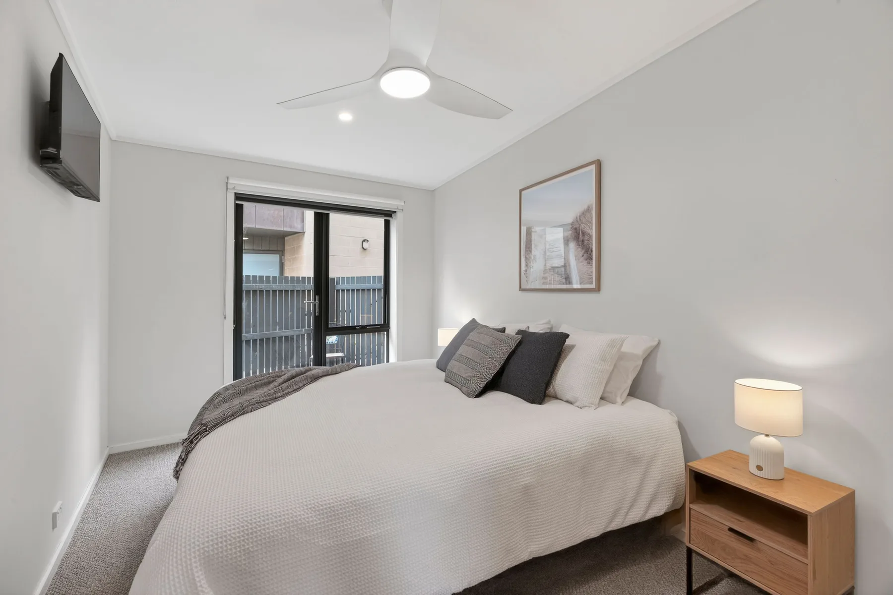 A bedroom with a neatly made bed, framed artwork, and a bedside table.