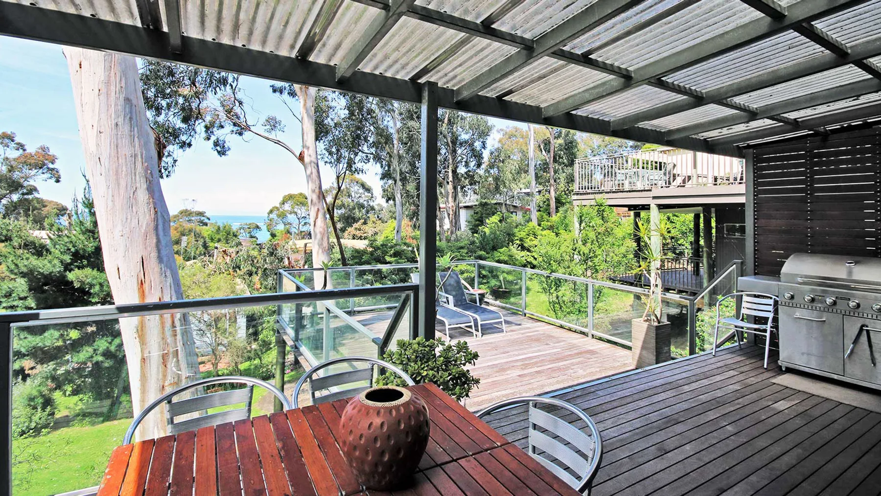 A covered outdoor deck with a dining table, grill, and views of greenery.