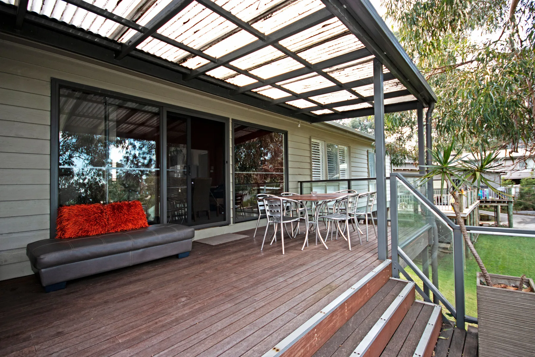 A covered wooden deck with outdoor seating beside glass doors.