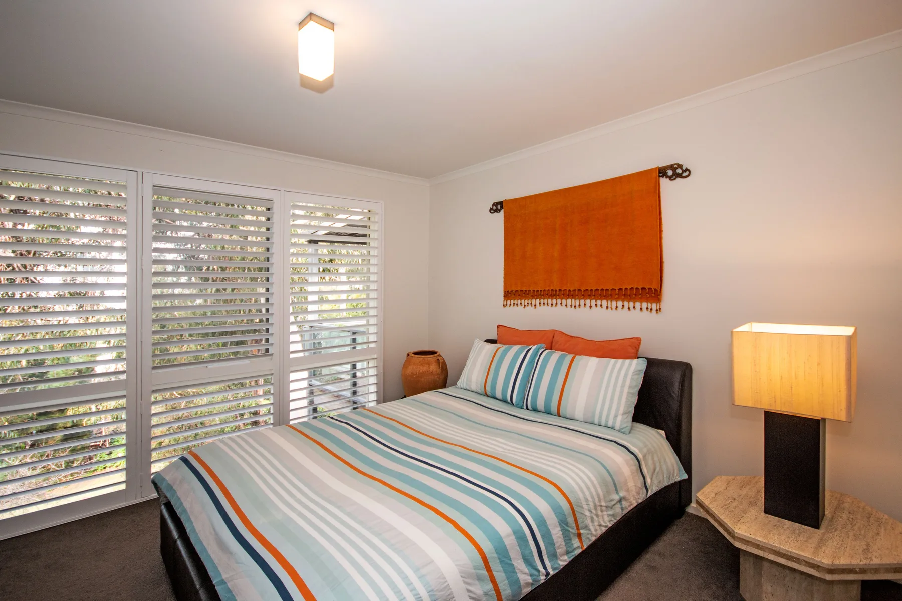 A bedroom with a neatly made bed and wide shuttered windows.