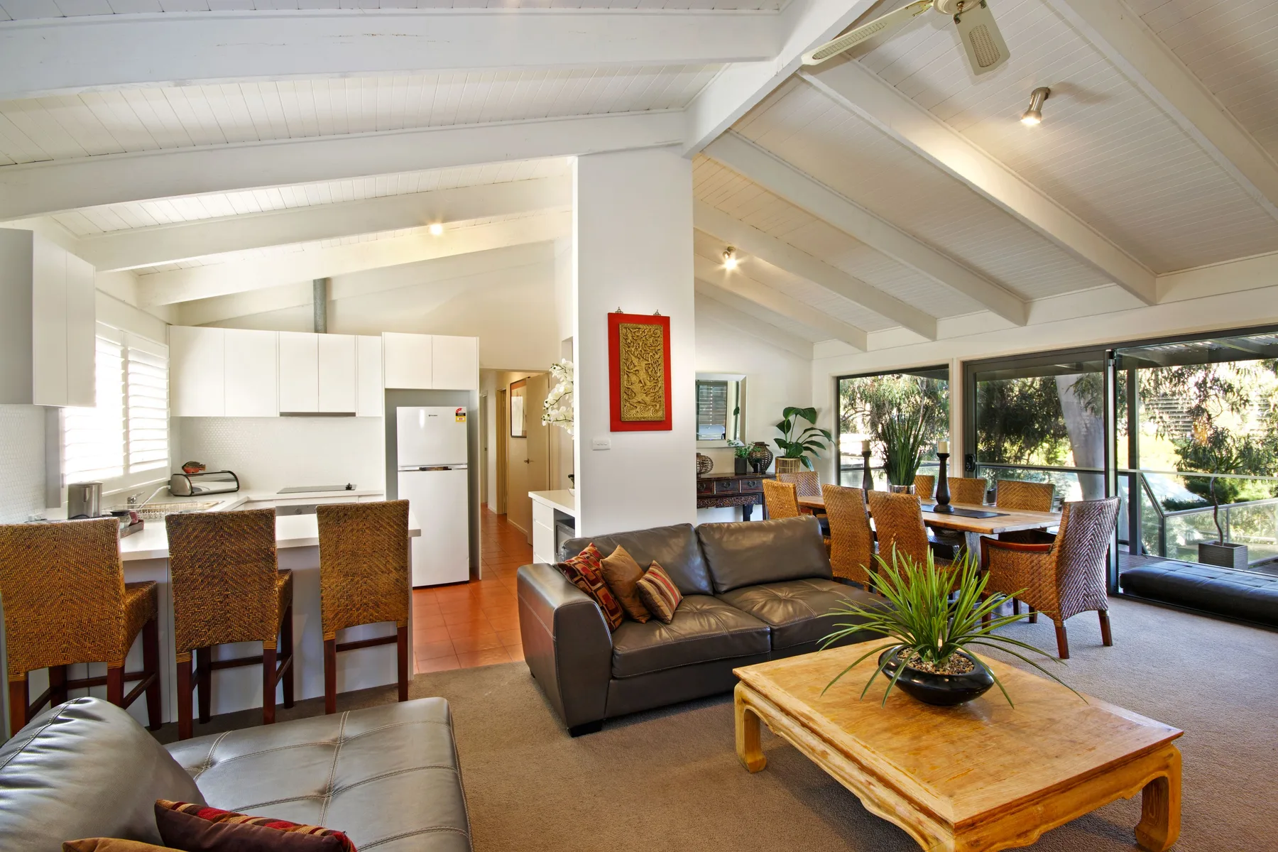 A bright open-plan living room and kitchen with seating beside large windows.