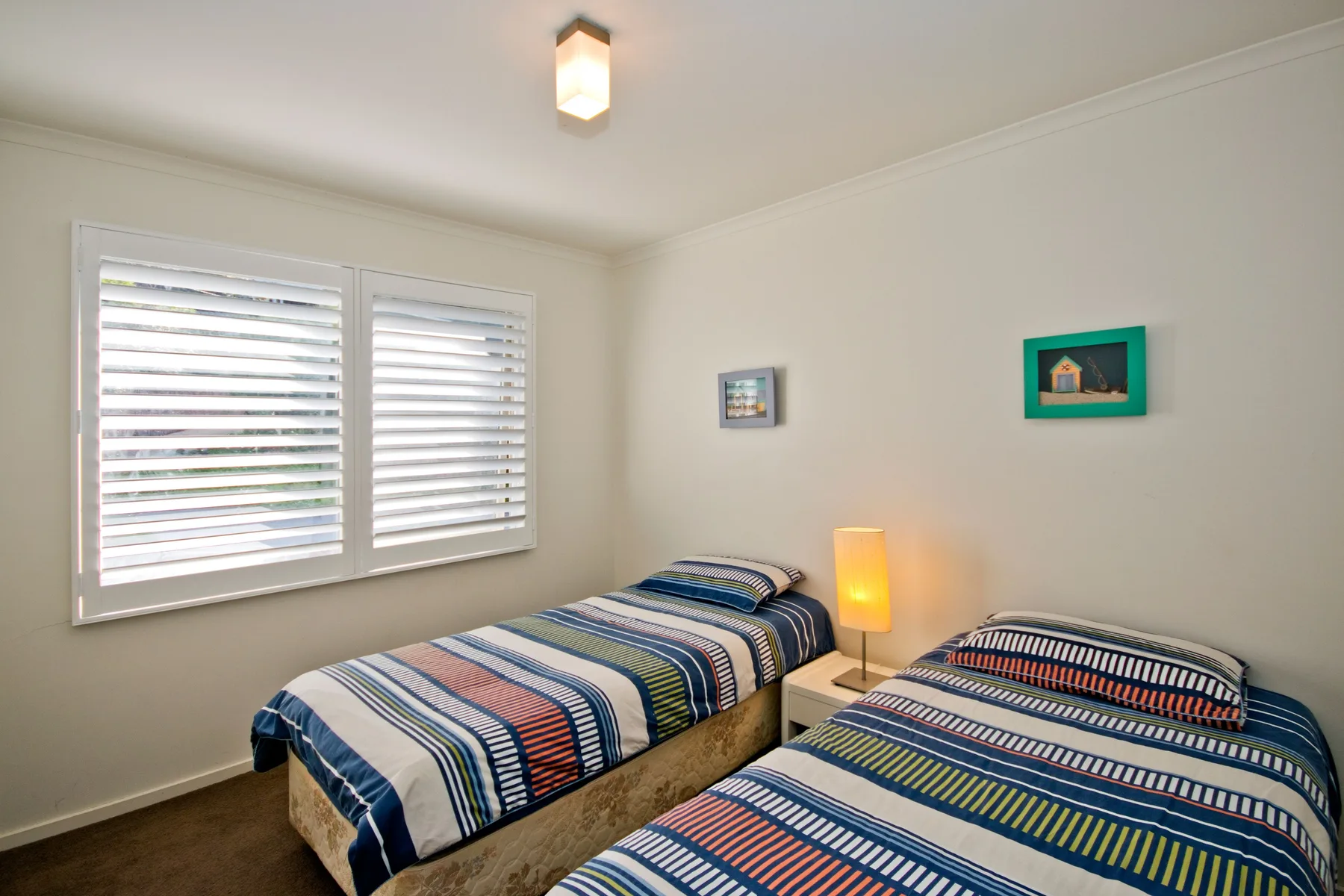 A bedroom with two beds dressed in striped bedding beside shuttered windows.