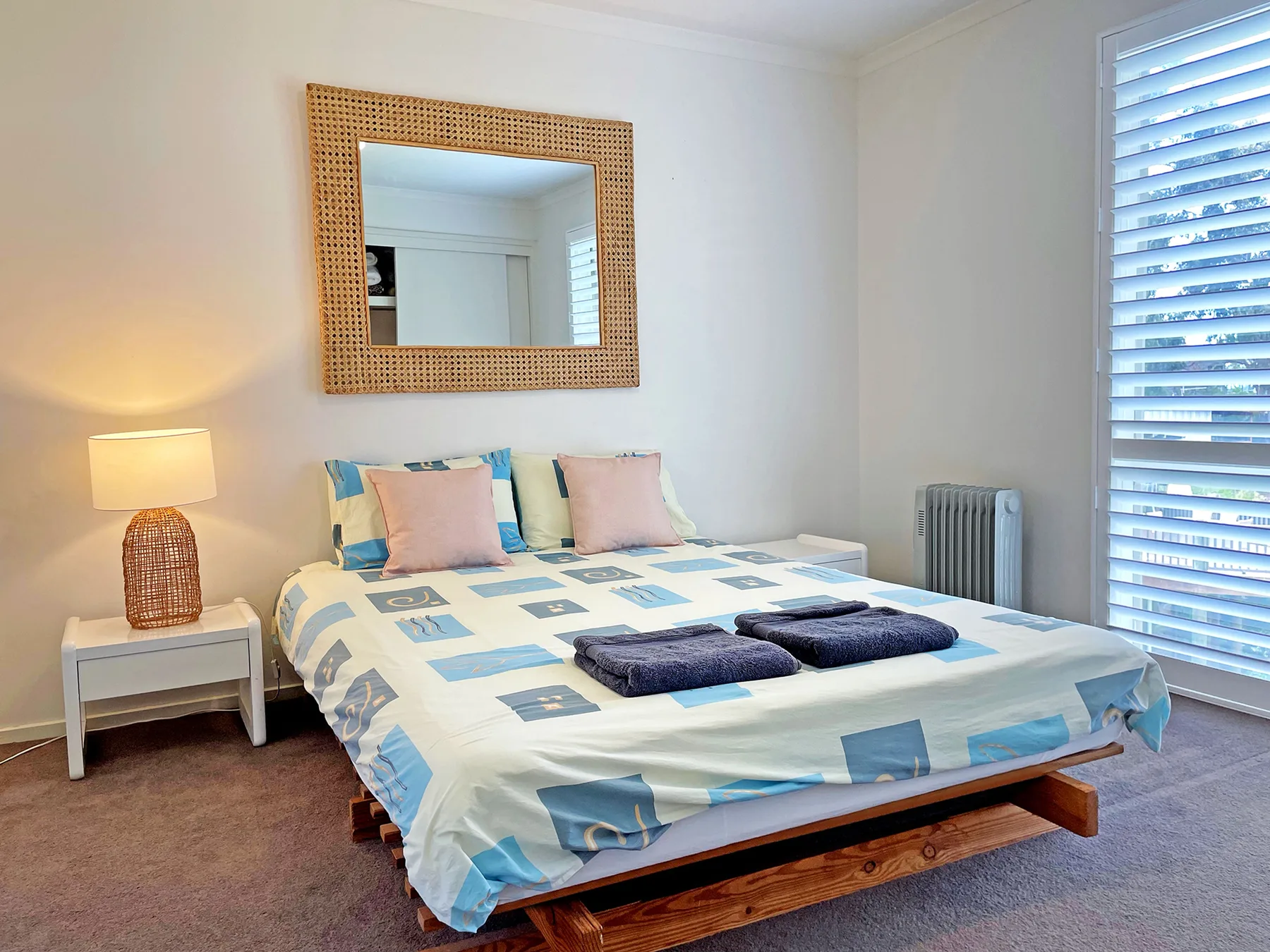 A bedroom with a bed, bedside table, and window blinds.