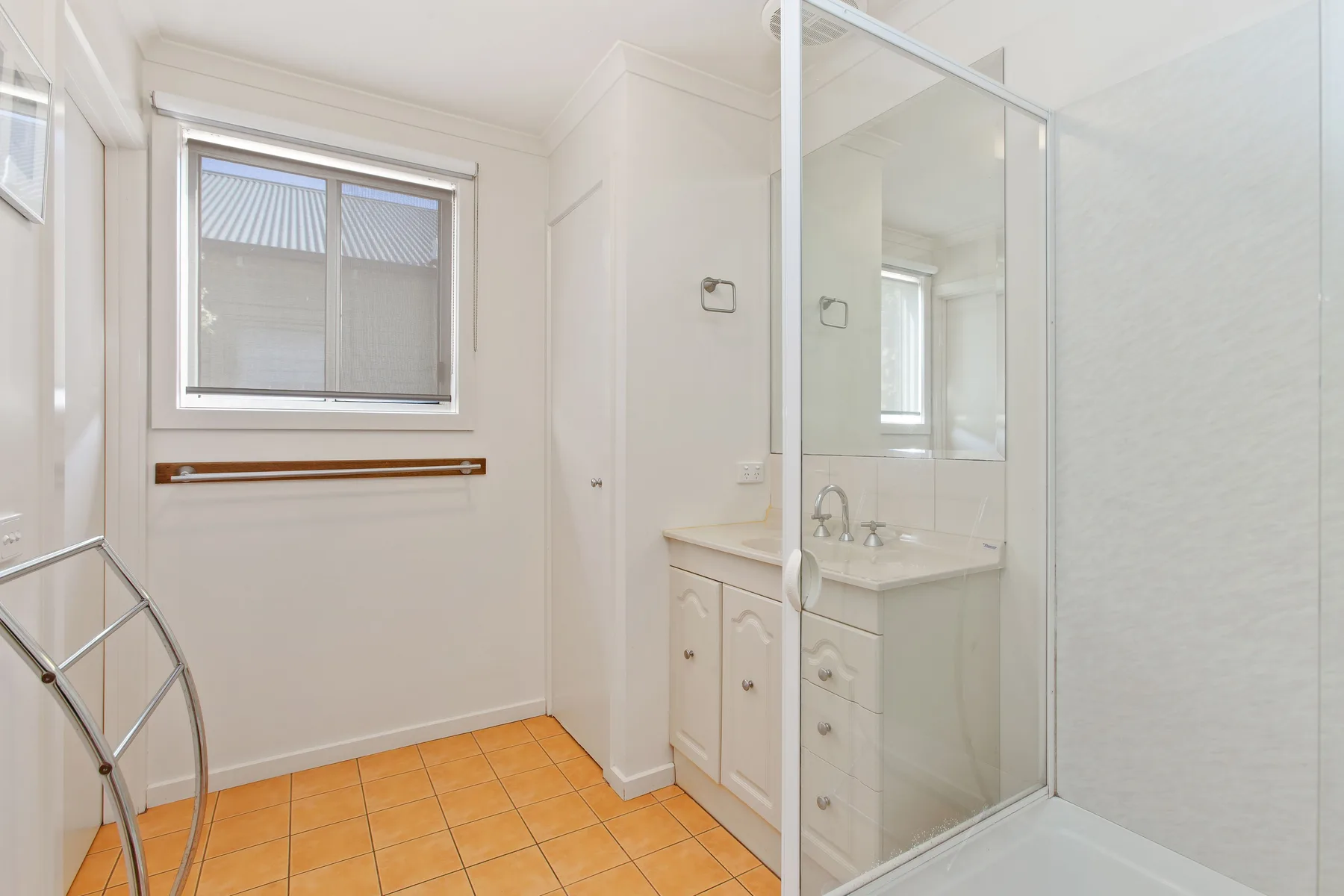 Un baño luminoso con ventana, lavabo y ducha de vidrio.