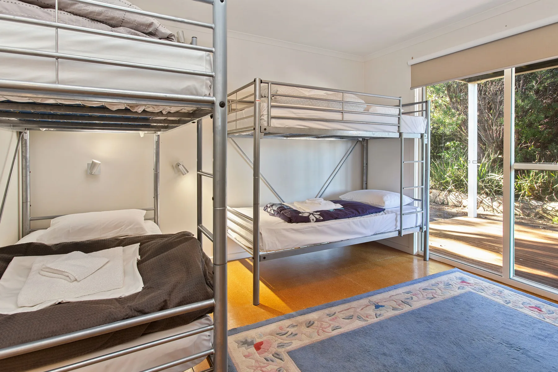 Un dormitorio con literas metálicas y grandes ventanas frente a la vegetación.