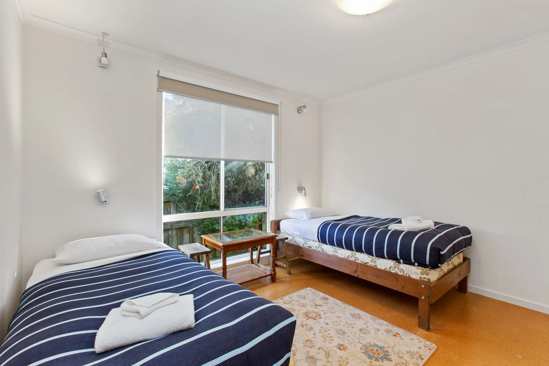 Un dormitorio luminoso con dos camas, una ventana grande y una alfombra estampada.