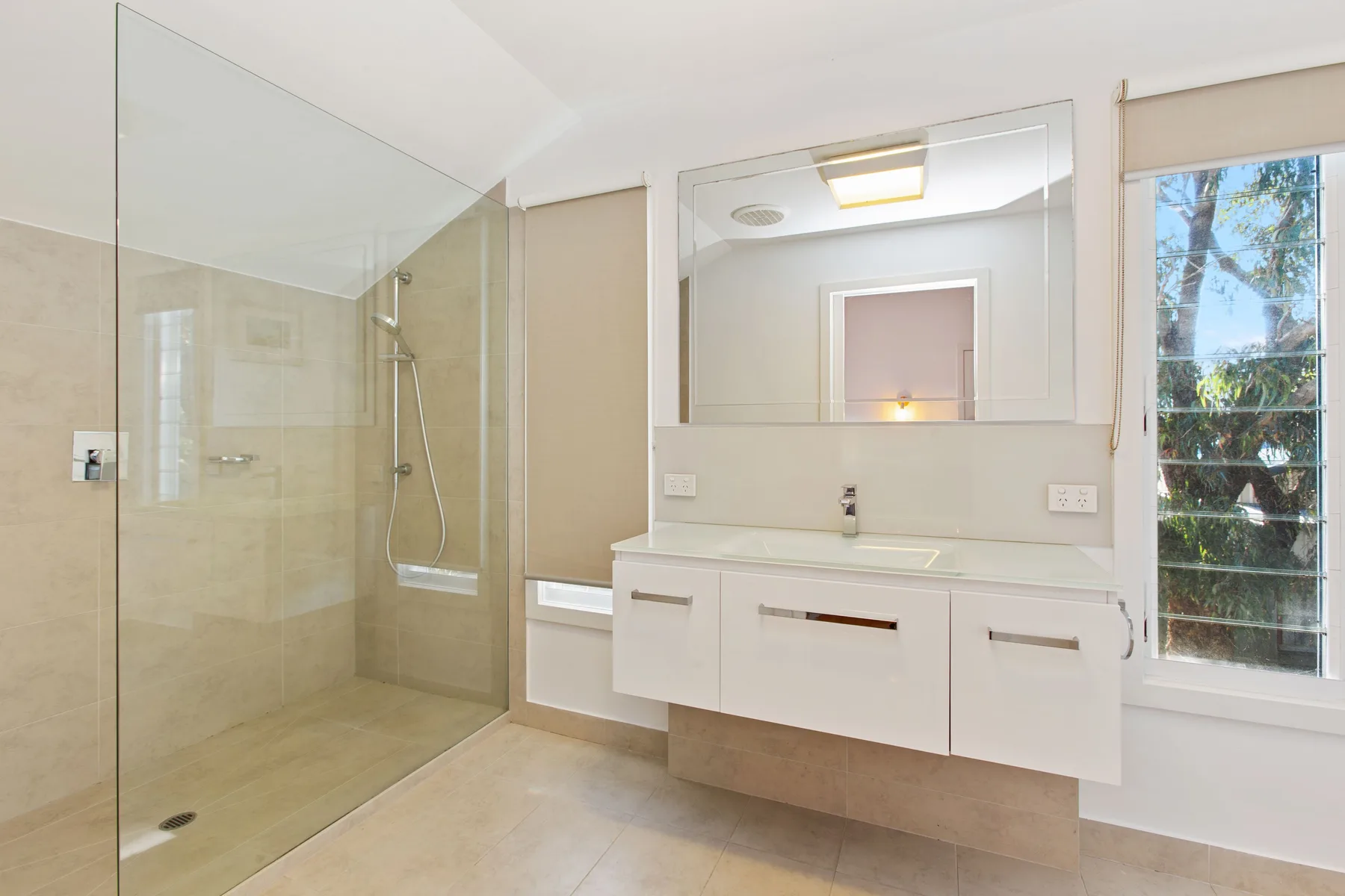 Un baño luminoso con una ducha de vidrio y un lavabo suspendido.